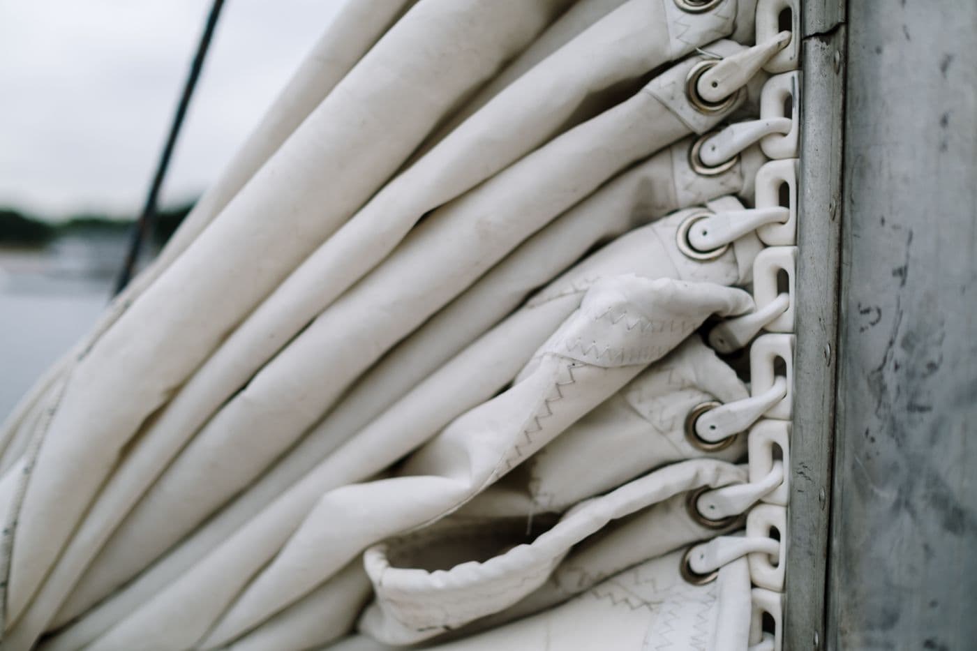 Stitched canvas sail cover folded along a boom with rings and fasteners