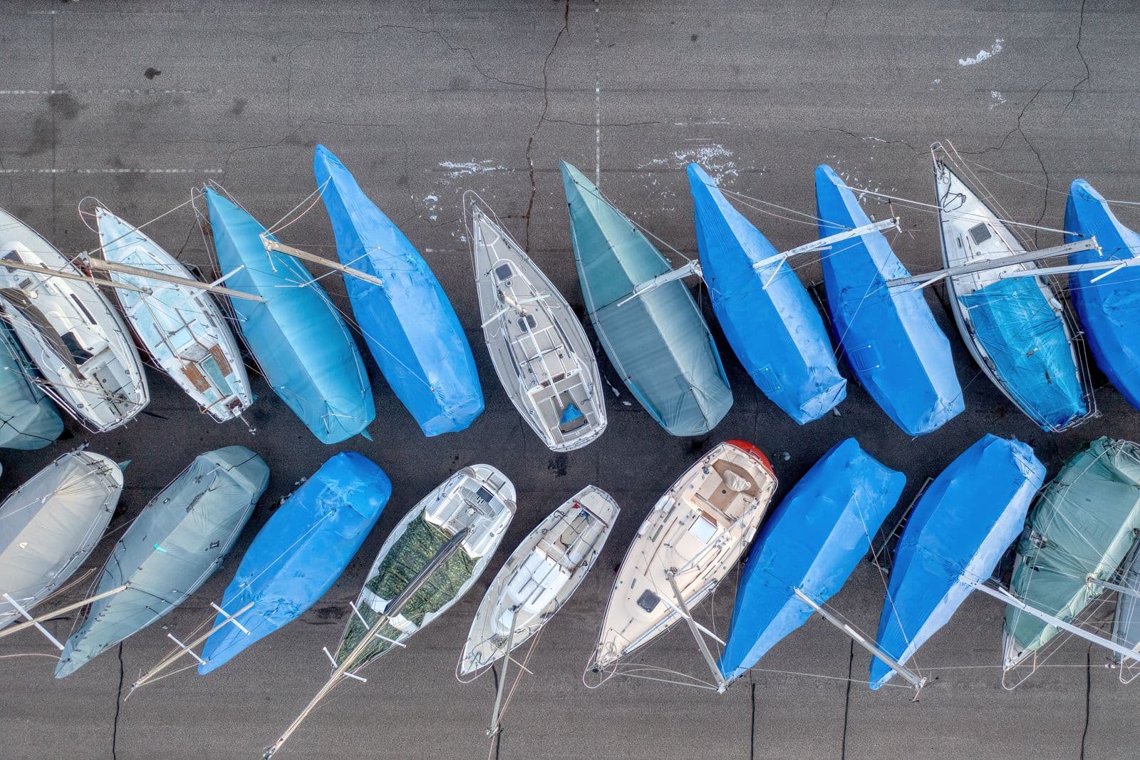 Rows of sailboats in storage, each wearing its own fitted fabric cover